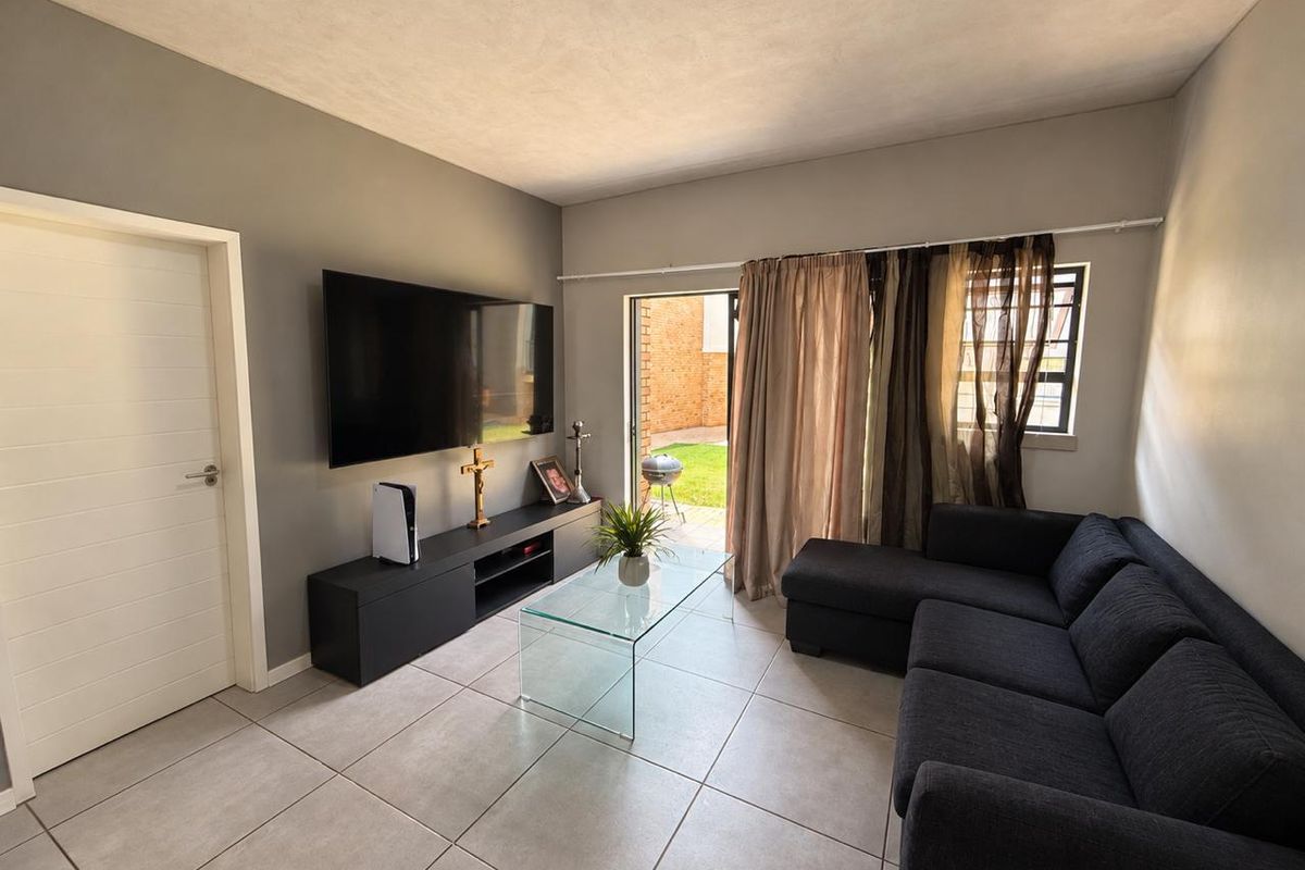 A well-maintained living room featuring neutral tiled flooring and direct access to an outdoor patio area through a sliding glass door.