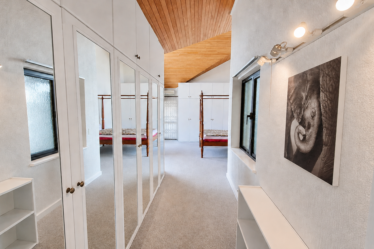 Spacious bedroom featuring a high vaulted timber ceiling, extensive built-in mirrored wardrobes, and integrated track lighting.