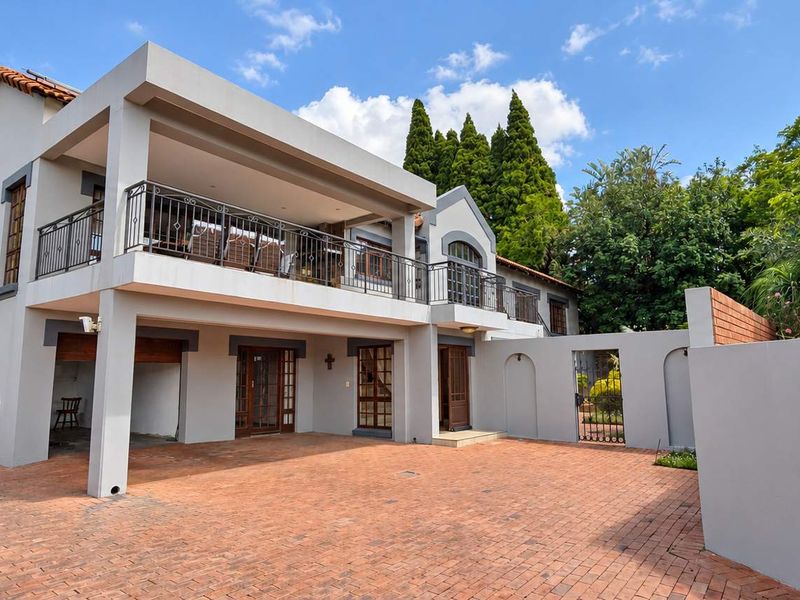 A well-maintained double-story house featuring a brick-paved driveway, a spacious covered patio, and a classic balcony with wrought iron railings.