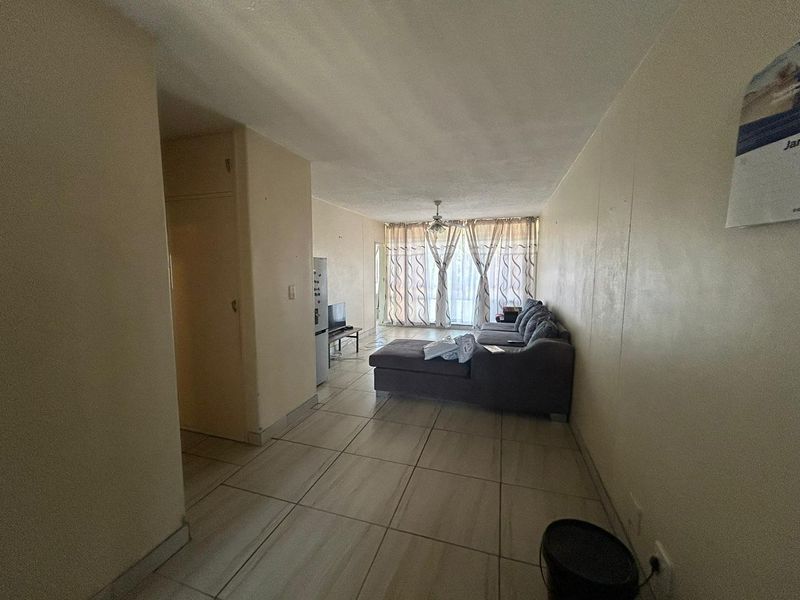 A spacious open-plan living area featuring tiled flooring, a ceiling fan, and large windows providing natural light.