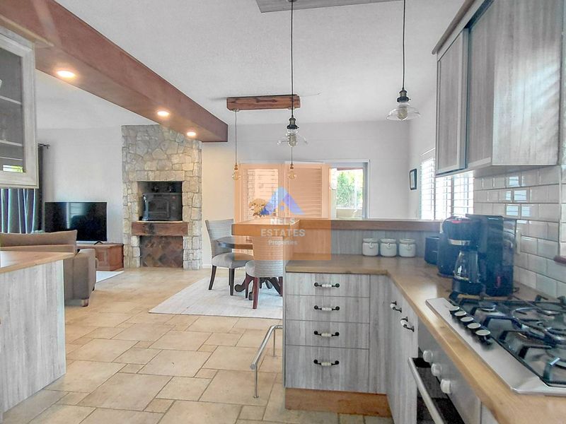 Spacious open-plan kitchen and living area featuring a stone fireplace, modern cabinetry, gas hob, and tiled flooring, creating a warm and functional living space.