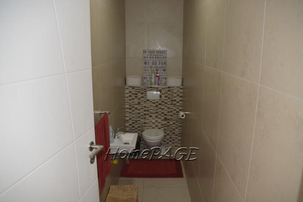 A compact guest bathroom featuring floor-to-ceiling wall tiles, a wall-mounted basin, and a toilet with a decorative mosaic tile feature wall.