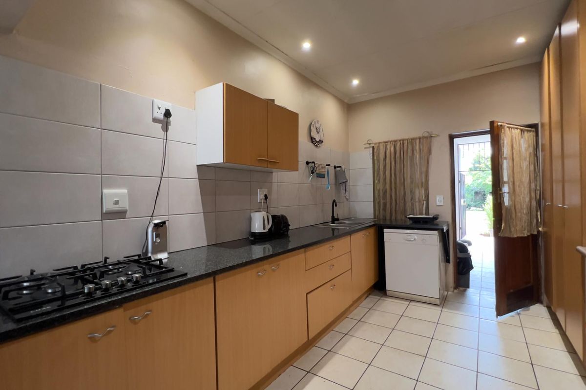 Functional kitchen featuring light wood cabinetry, granite countertops, a gas hob, and tiled flooring with direct access to the exterior.