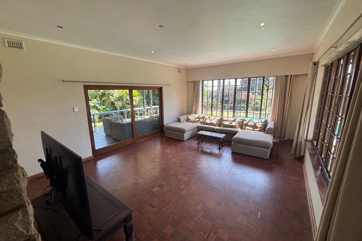 Spacious living room featuring classic parquet flooring, large windows, and sliding glass doors providing direct access to the outdoor patio area.