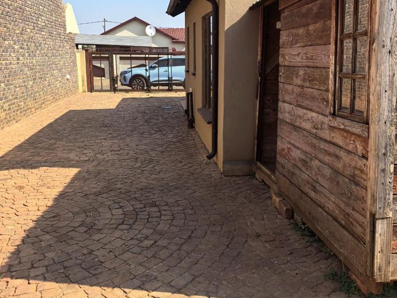 A side exterior view of the property featuring cobblestone paving, a brick boundary wall, and a timber-clad structure.