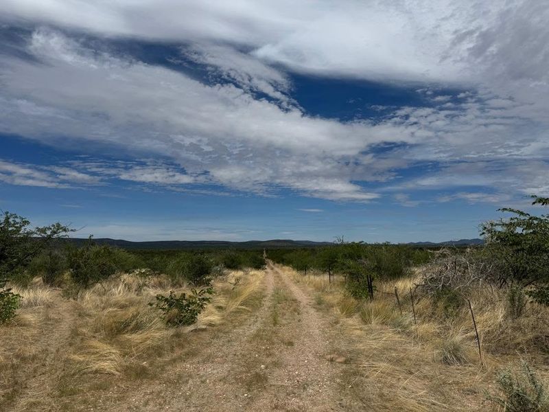 A scenic view of the expansive farm landscape featuring a dirt access track and wire fencing under a cloudy sky.