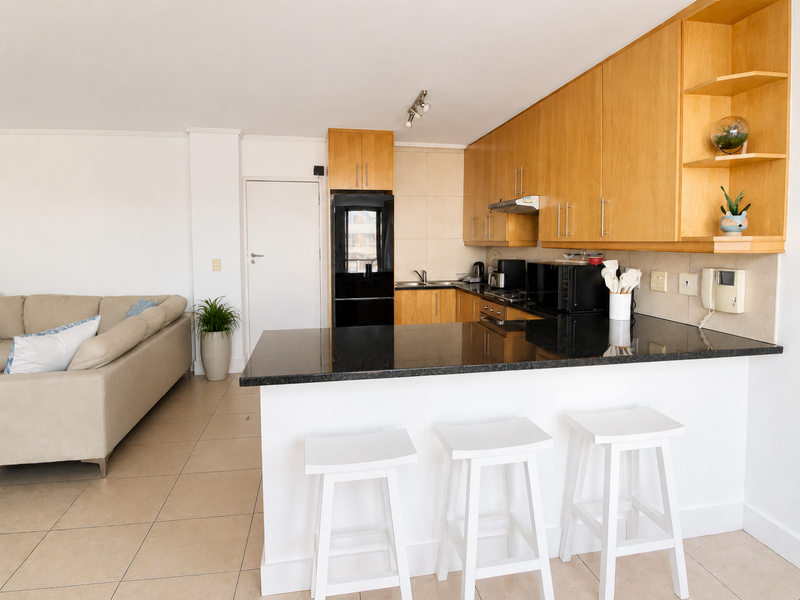 Open-plan kitchen featuring light wood cabinetry, black granite countertops, and a breakfast bar, seamlessly integrated with the adjacent living area.