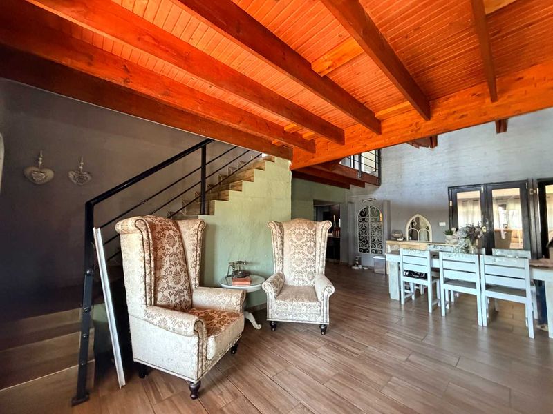 Spacious open-plan living and dining area featuring high exposed timber beam ceilings, tiled flooring, and a feature staircase with metal balustrades.