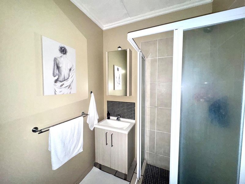 Compact bathroom featuring a vanity basin, medicine cabinet, and a corner shower enclosure with tiled surrounds.