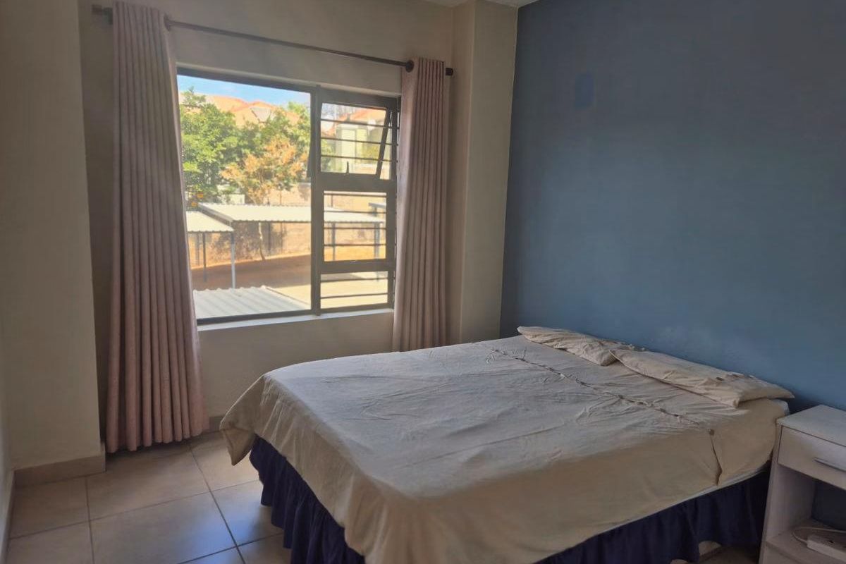 A bedroom featuring tiled flooring, a large window with curtains, and a blue accent wall.