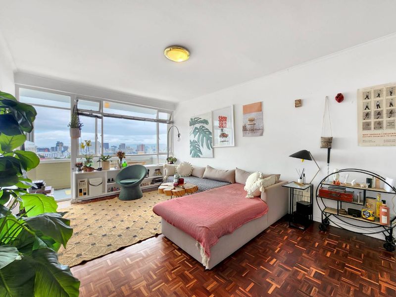 Bright living room featuring classic parquet flooring and expansive floor-to-ceiling windows offering panoramic city views.