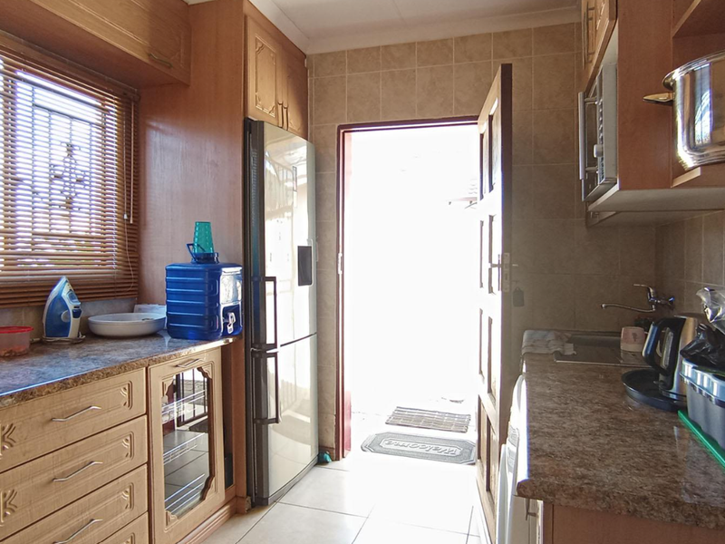 A functional kitchen featuring laminate cabinetry, tiled backsplash, and tiled flooring, with direct access to the exterior.