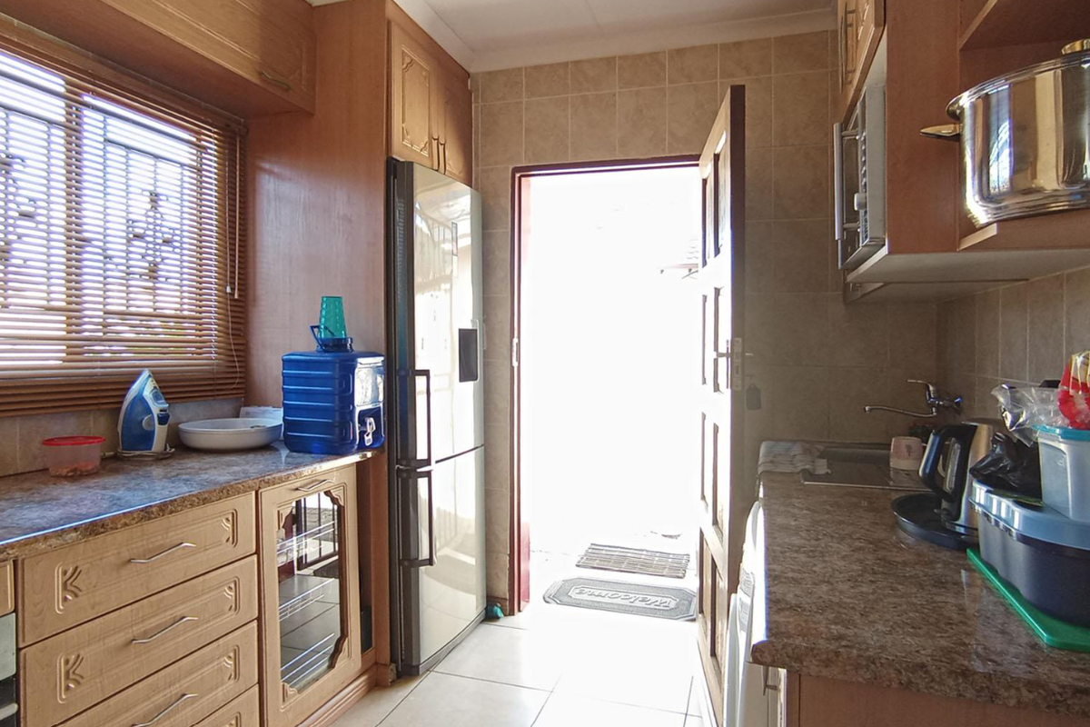 A functional kitchen featuring laminate cabinetry, tiled backsplash, and tiled flooring, with direct access to the exterior.