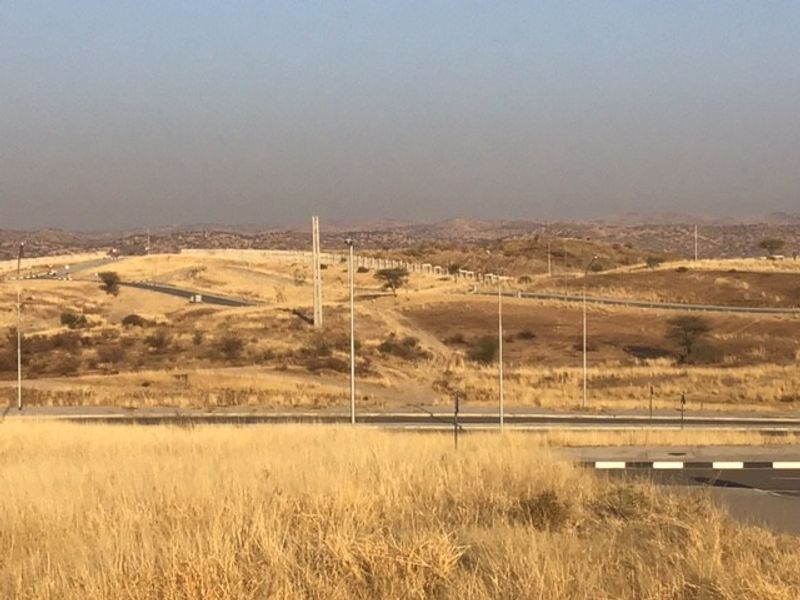 An elevated view of a vacant commercial land plot featuring paved road access, street lighting infrastructure, and surrounding hilly landscape.