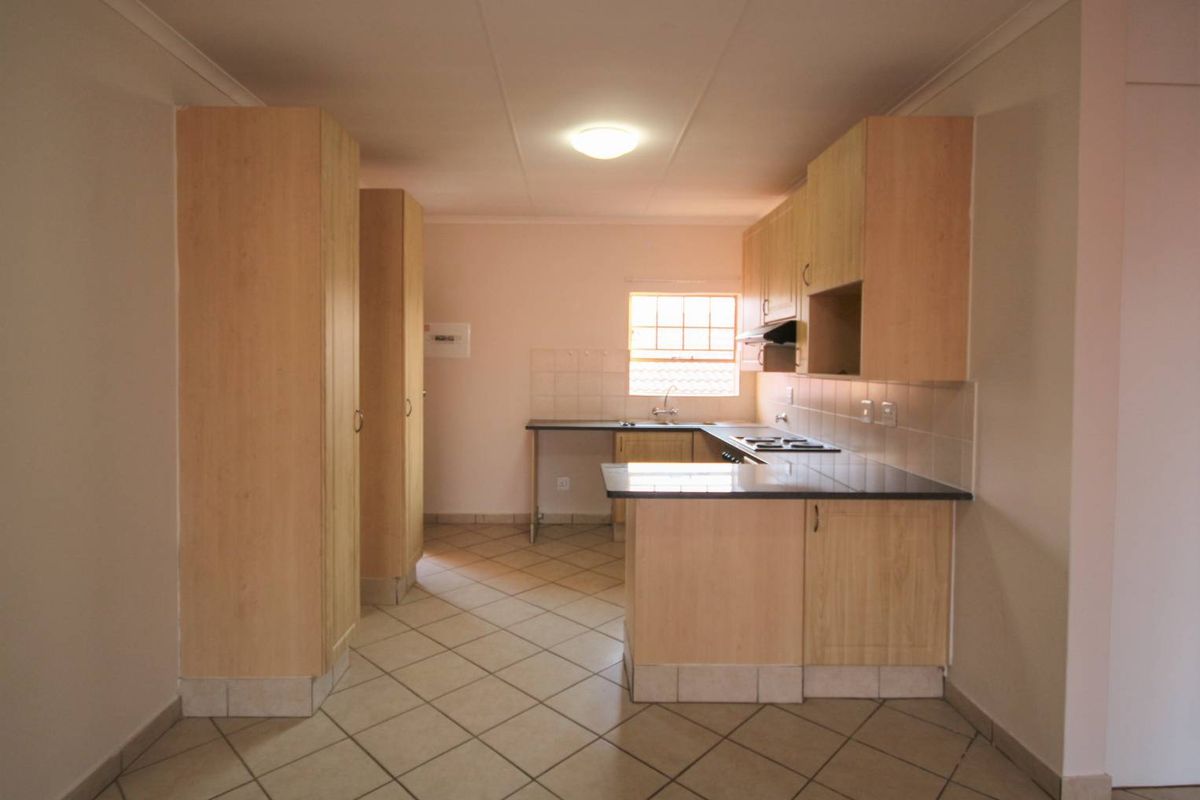 A functional kitchen featuring light wood cabinetry, dark countertops, tiled flooring, and a built-in hob with an extractor fan.