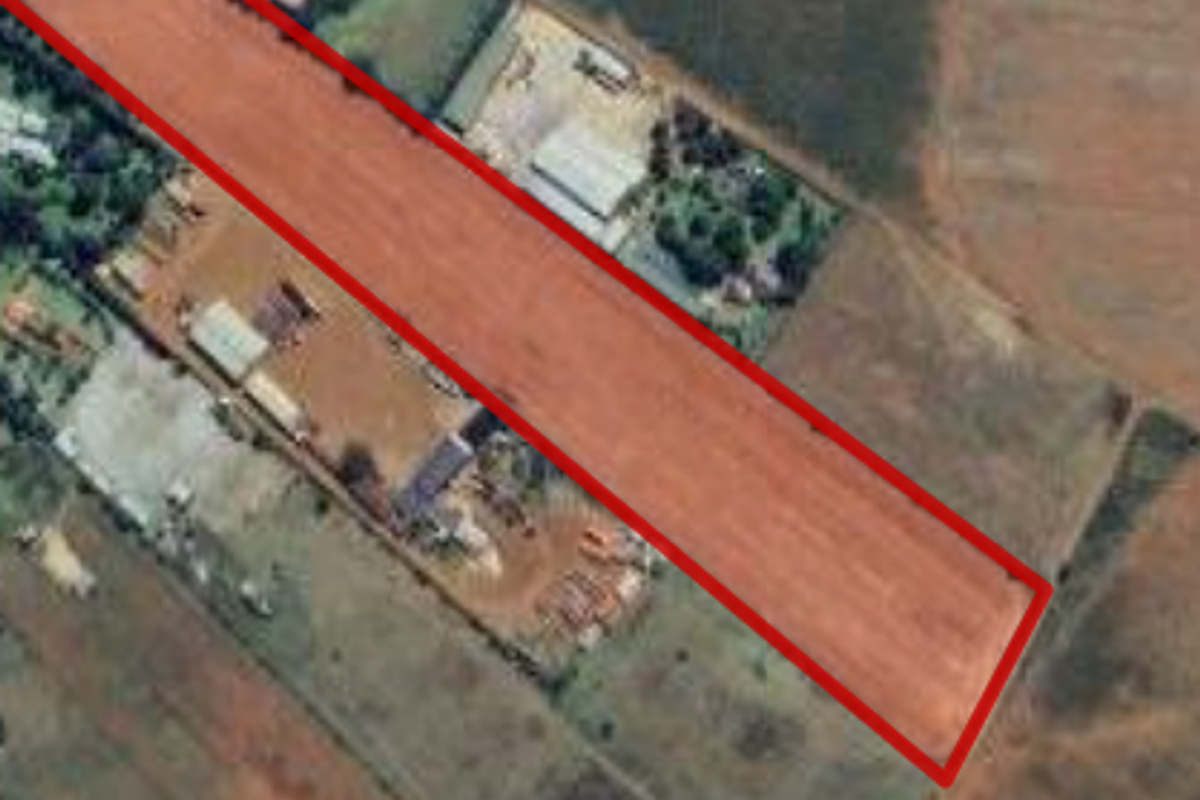 An aerial view of a vacant agricultural land plot, clearly outlined in red, showing the surrounding terrain and nearby structures.