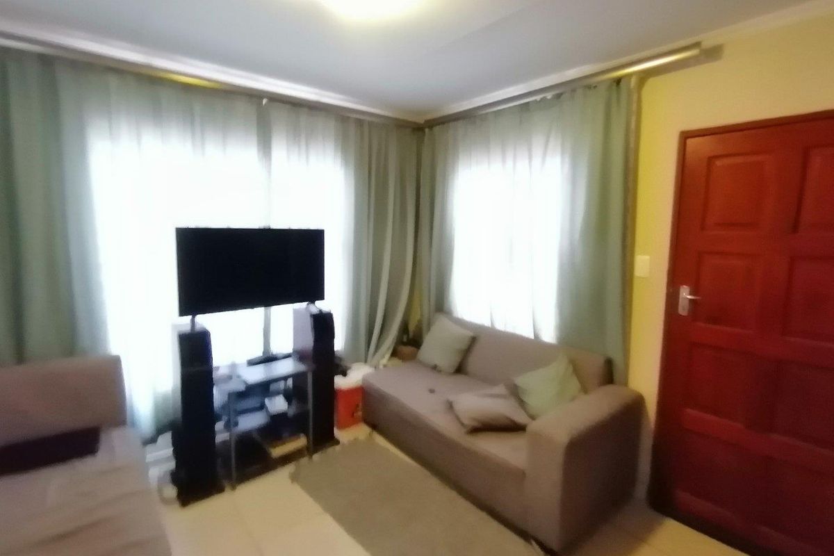 A living room featuring tiled flooring, large windows with curtain tracks, and a solid timber entrance door.