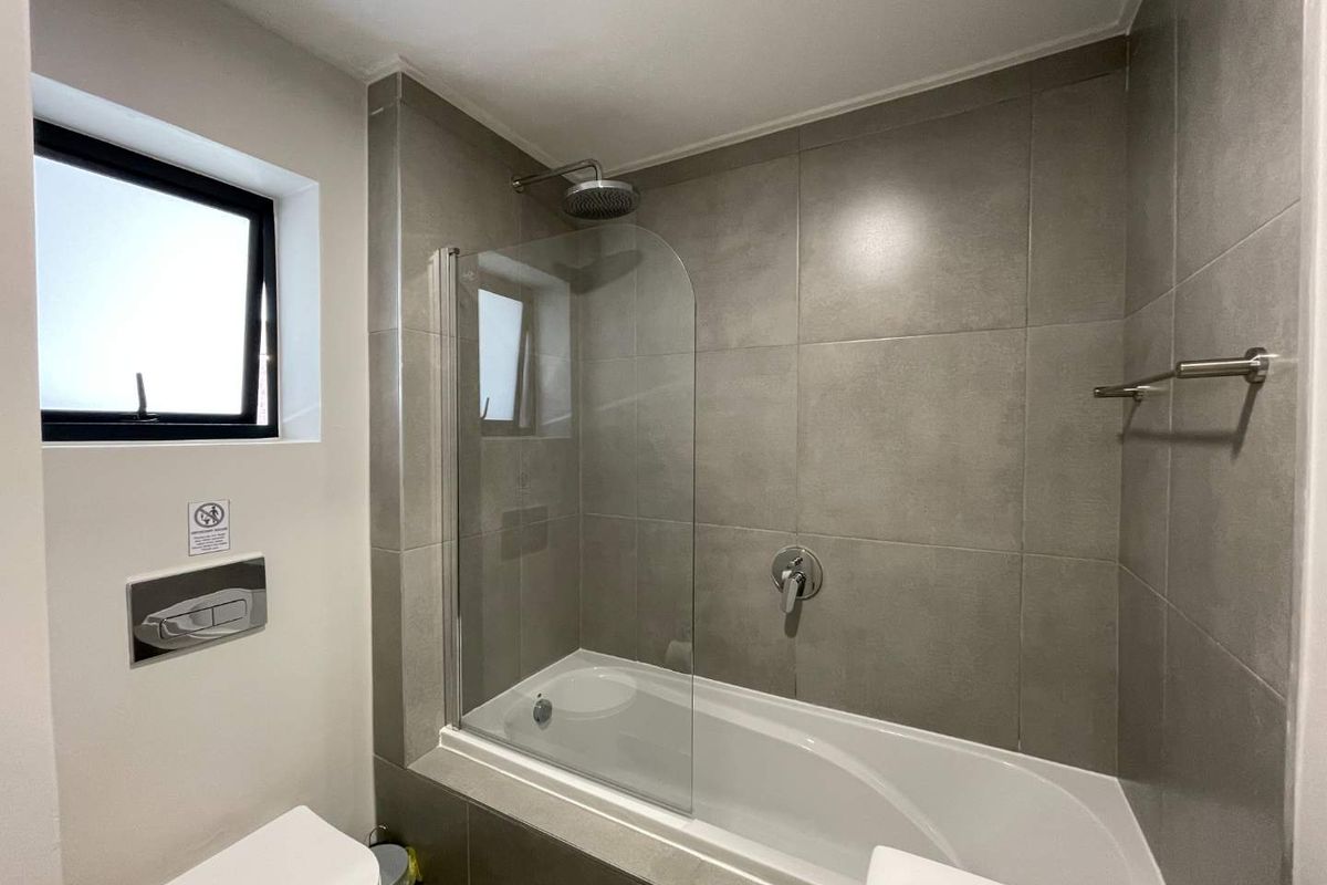 Modern bathroom featuring a tiled bathtub with a glass shower screen, wall-mounted toilet, and contemporary fixtures.