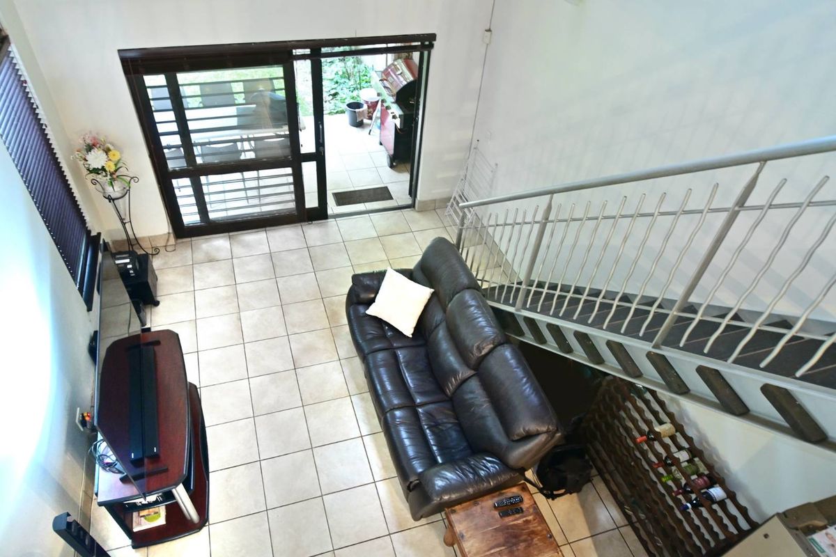 An elevated view of a living area featuring tiled flooring, a staircase with metal railings, and sliding glass doors leading to an outdoor patio.