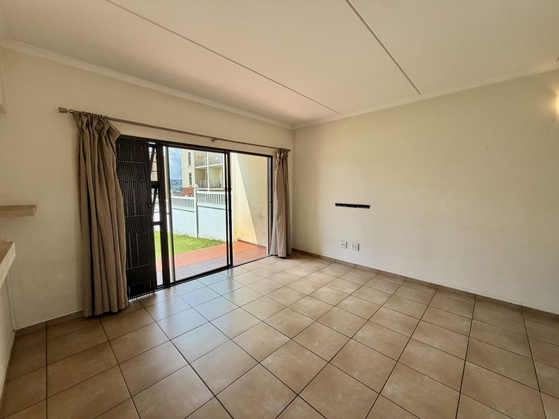 An empty, tiled living room featuring a sliding glass door with security gate, providing access to an outdoor patio area.