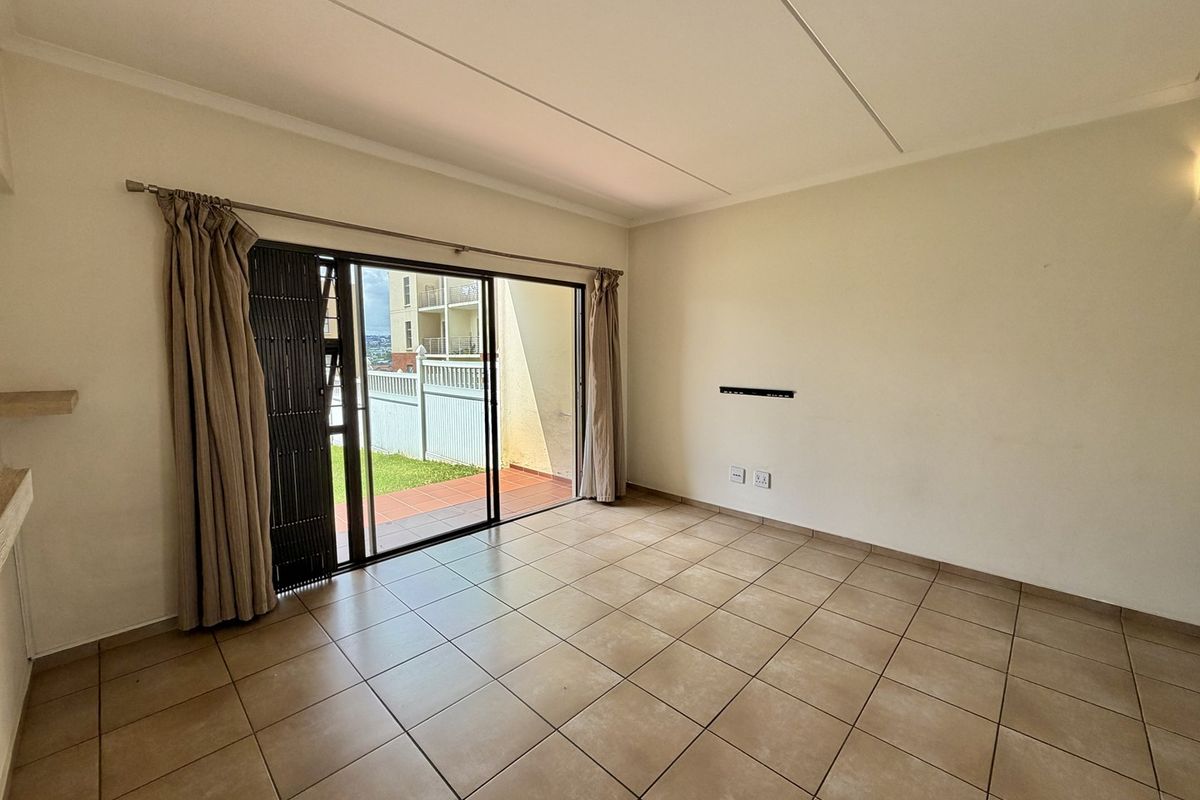 An empty, tiled living room featuring a sliding glass door with security gate, providing access to an outdoor patio area.
