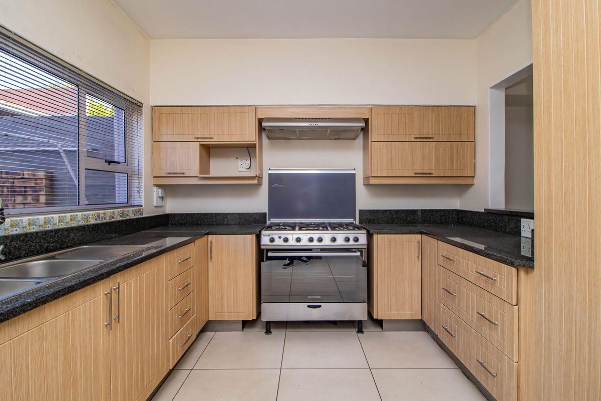 A clean, well-maintained kitchen featuring light-wood cabinetry, granite countertops, a stainless steel double sink, and a freestanding gas stove with an extractor fan.