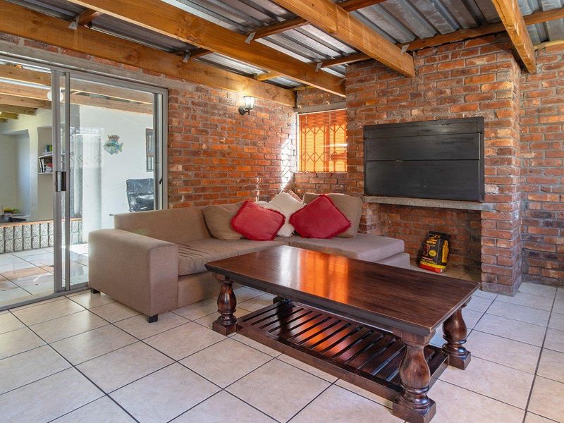 Covered patio area featuring exposed brick walls, timber beam ceiling, tiled flooring, and a built-in braai, providing a rustic outdoor entertainment space.