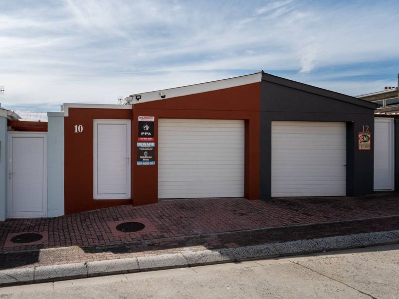 Front elevation of the property featuring a double garage with roller shutter doors and a paved driveway entrance.