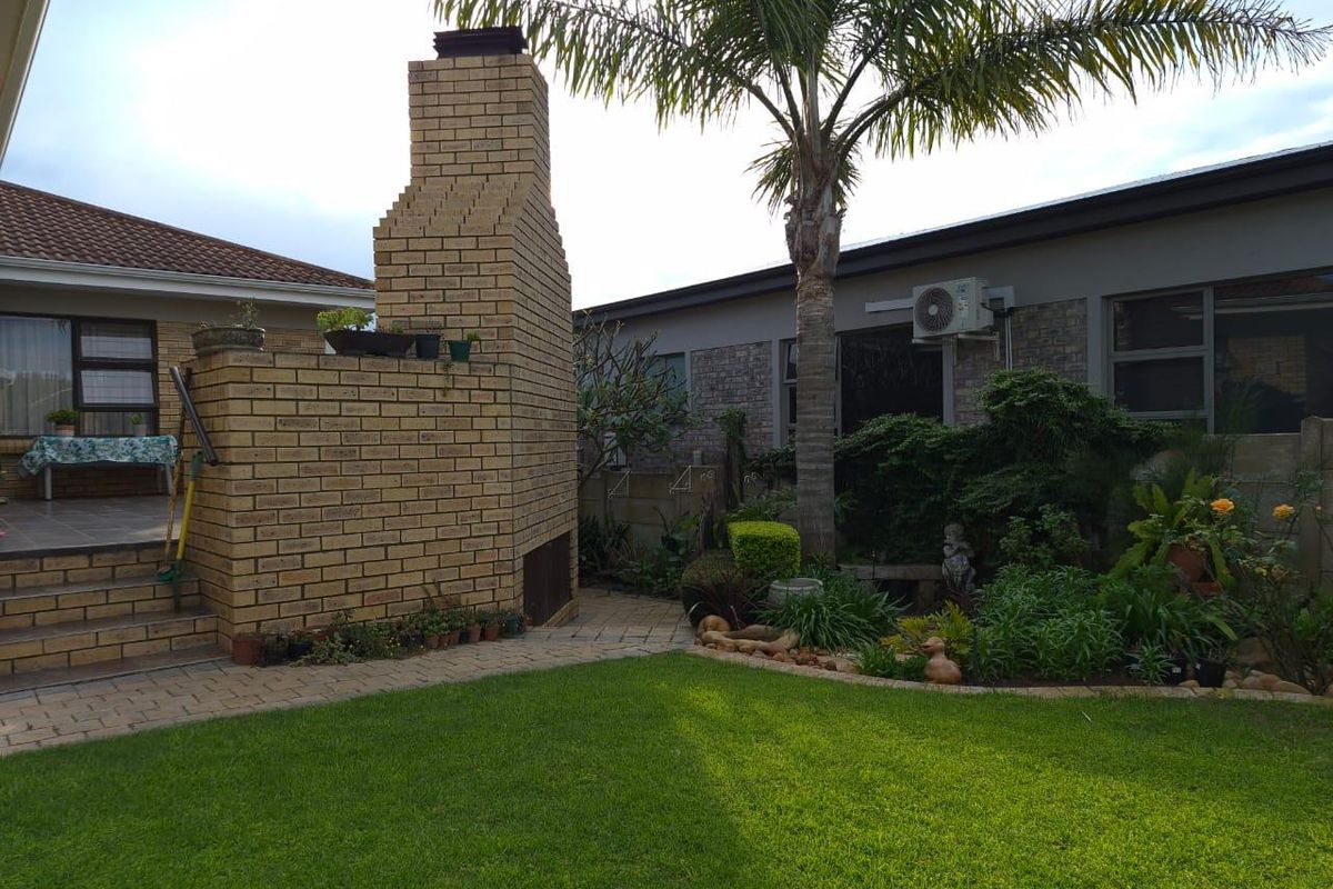 A private rear garden featuring a brick-built outdoor fireplace, paved patio area, established landscaping, and a well-maintained lawn.