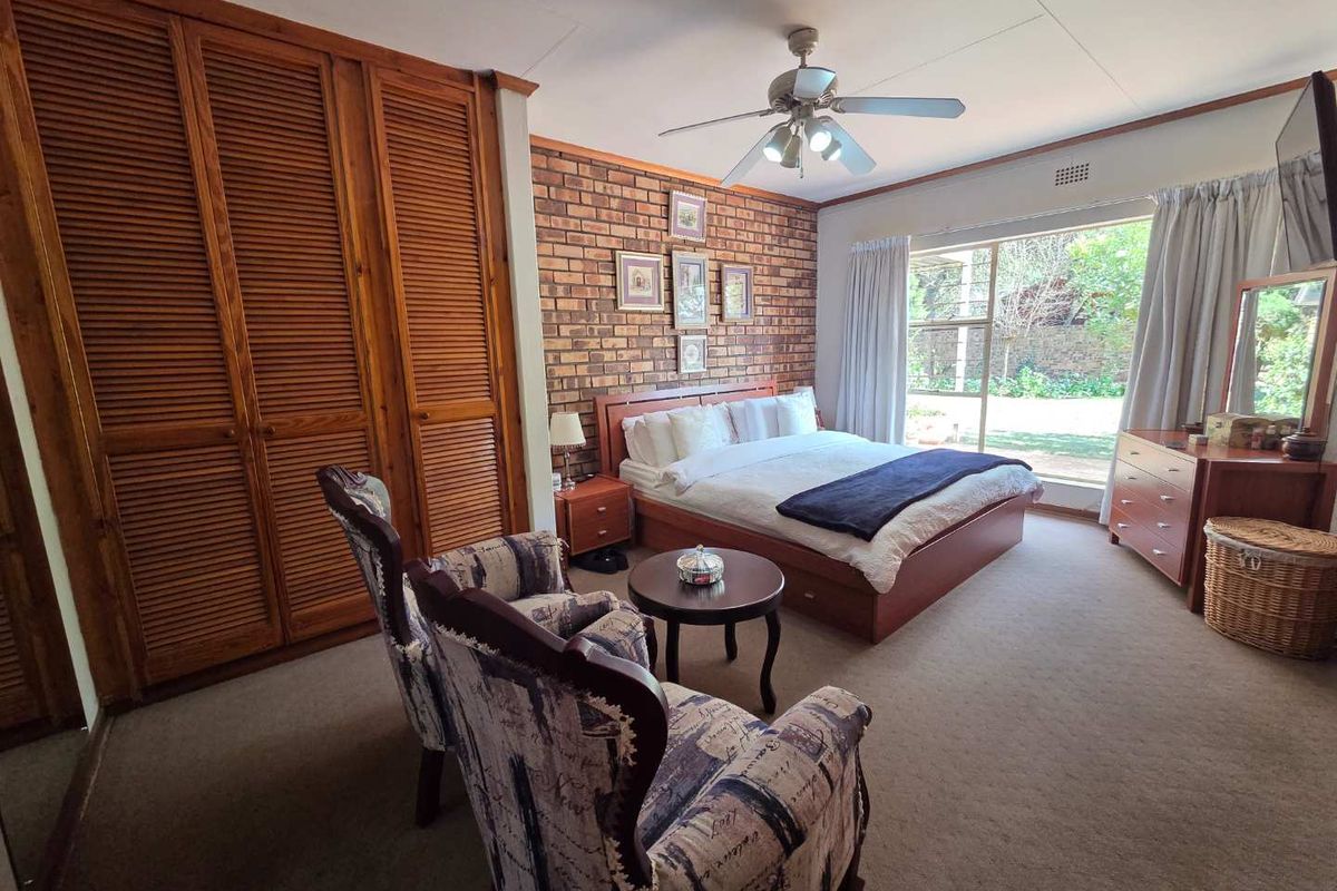 Spacious bedroom featuring an exposed brick wall, built-in wooden louvered wardrobes, a ceiling fan, and direct access to the garden through a sliding glass door.