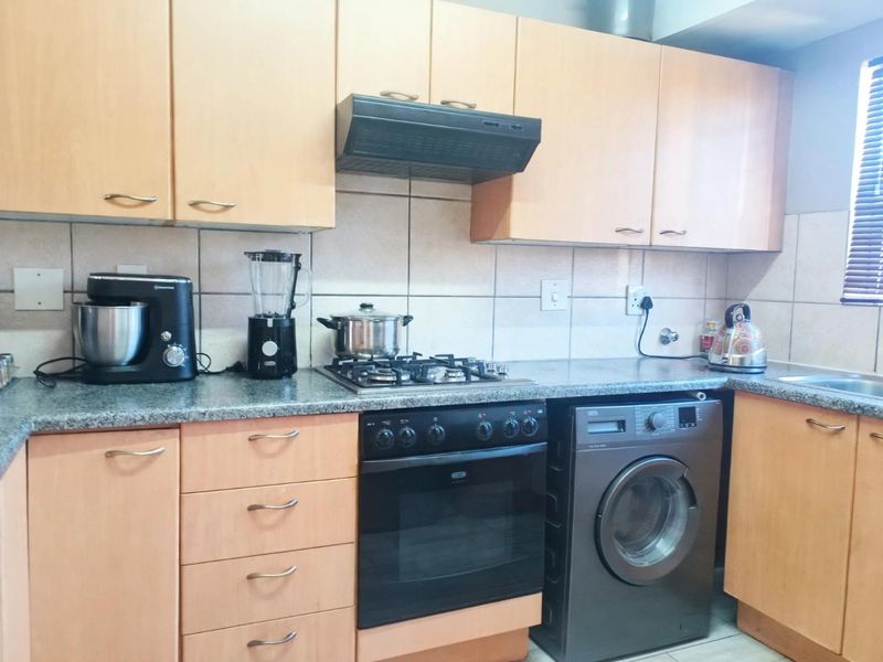 Functional kitchen featuring light wood cabinetry, granite countertops, a gas hob, built-in oven, and an integrated washing machine.