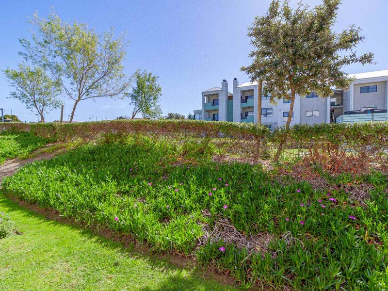 A view of the apartment complex exterior featuring well-maintained landscaped gardens, lawn areas, and mature trees.
