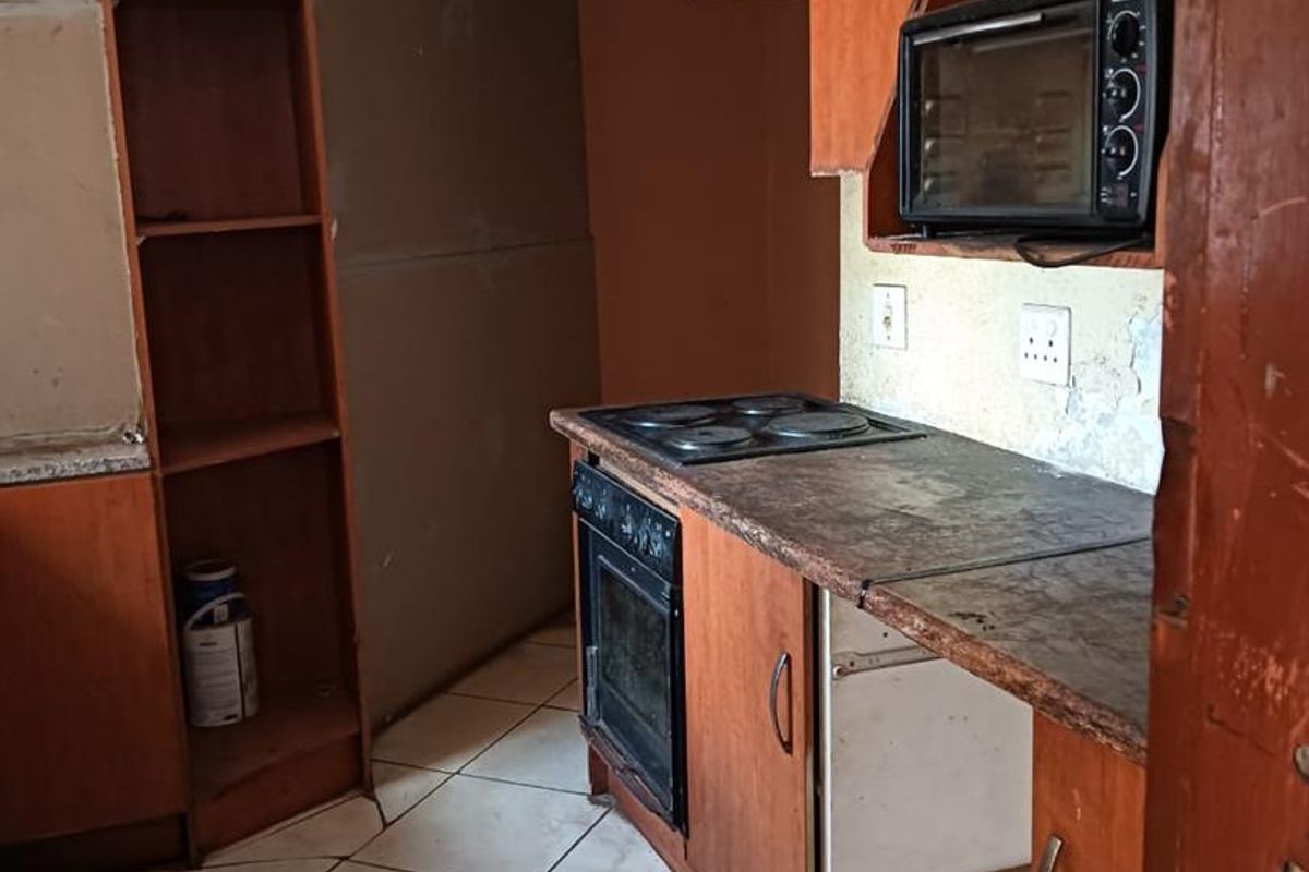 A dated kitchen featuring wood-finish cabinetry, a built-in oven and hob, and tiled flooring, currently requiring significant maintenance and cosmetic updates.