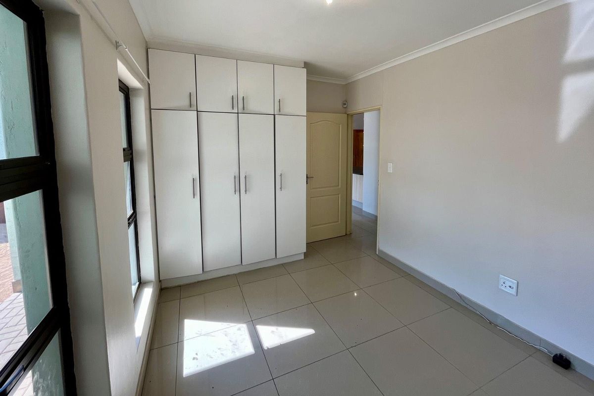A bright bedroom featuring neutral tiled flooring, built-in white cabinetry, and a large window providing natural light.