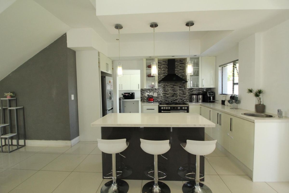 Modern kitchen featuring a central island with breakfast bar, sleek cabinetry, tiled backsplash, and built-in stove with extractor fan.