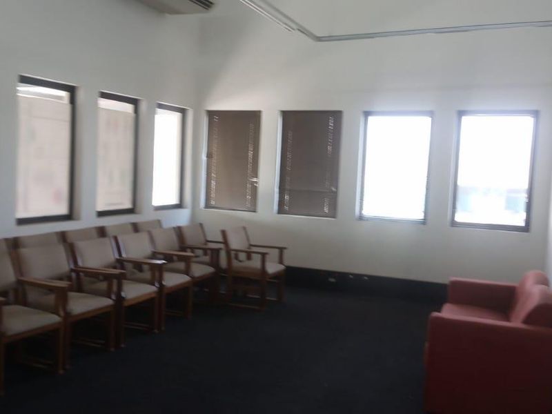 A functional office or waiting area featuring multiple windows, neutral walls, and dark carpeting, suitable for professional use or conversion.