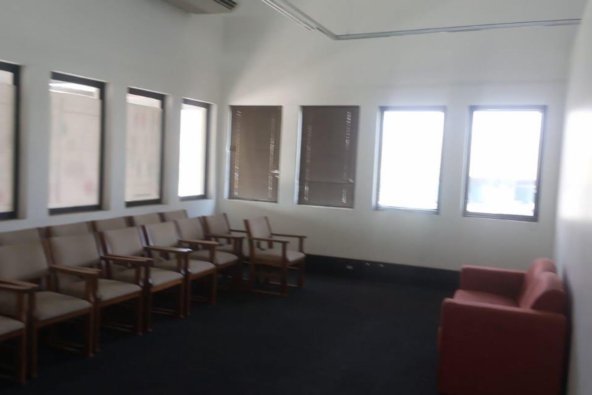 A functional office or waiting area featuring multiple windows, neutral walls, and dark carpeting, suitable for professional use or conversion.
