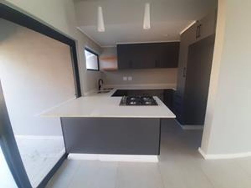 Modern kitchen featuring dark cabinetry, stone countertops, integrated gas hob, and direct access to the outdoor area through a large sliding glass door.