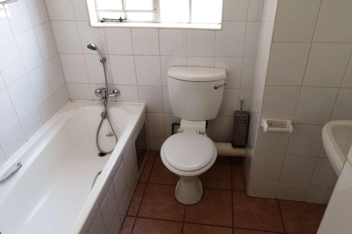 A functional bathroom featuring a standard bathtub with handheld shower mixer, toilet, and tiled finishes throughout.