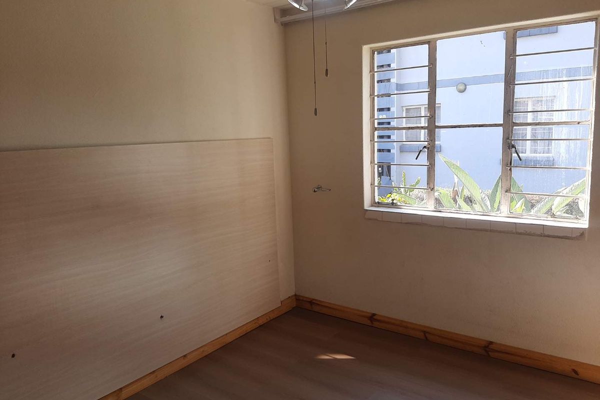 An empty bedroom featuring laminate flooring, timber skirting boards, and a steel-framed window with security bars, offering a blank canvas for renovation.