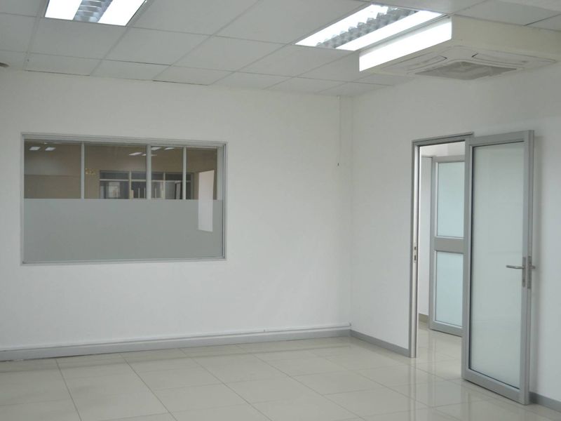 A clean, vacant office space featuring neutral ceramic tiling, suspended ceilings with integrated lighting, and modern aluminium-framed glass partitioning.