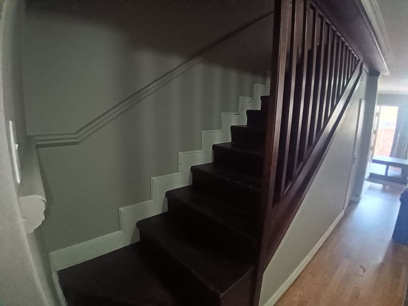 A hallway featuring a wooden staircase with a matching balustrade and laminate flooring, leading towards an open living area.
