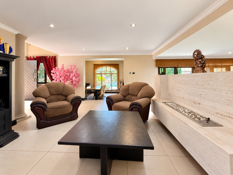 Spacious living room featuring a prominent travertine fireplace surround, recessed lighting, and large format floor tiles, leading through an archway to the dining area.