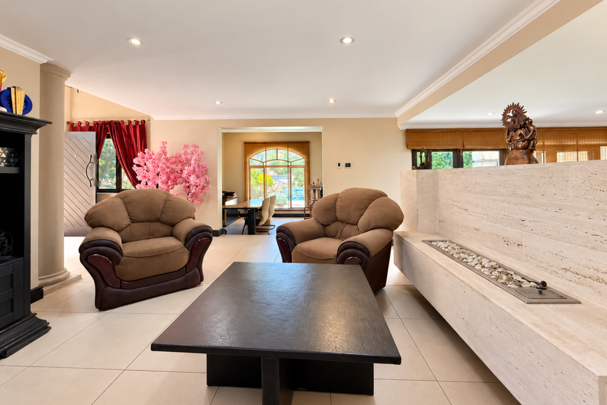 Spacious living room featuring a prominent travertine fireplace surround, recessed lighting, and large format floor tiles, leading through an archway to the dining area.