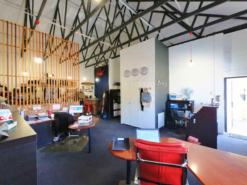 Spacious industrial-style office featuring high vaulted ceilings with exposed steel trusses, timber slat partitioning, and functional built-in storage.