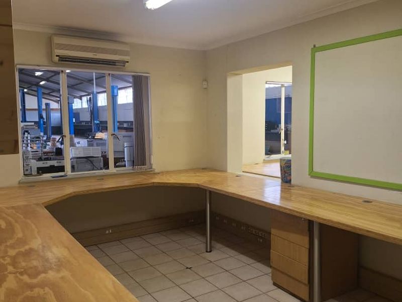 Functional office space featuring a large built-in wooden desk, tiled flooring, and a wall-mounted air conditioning unit, suitable for administrative or industrial workspace use.