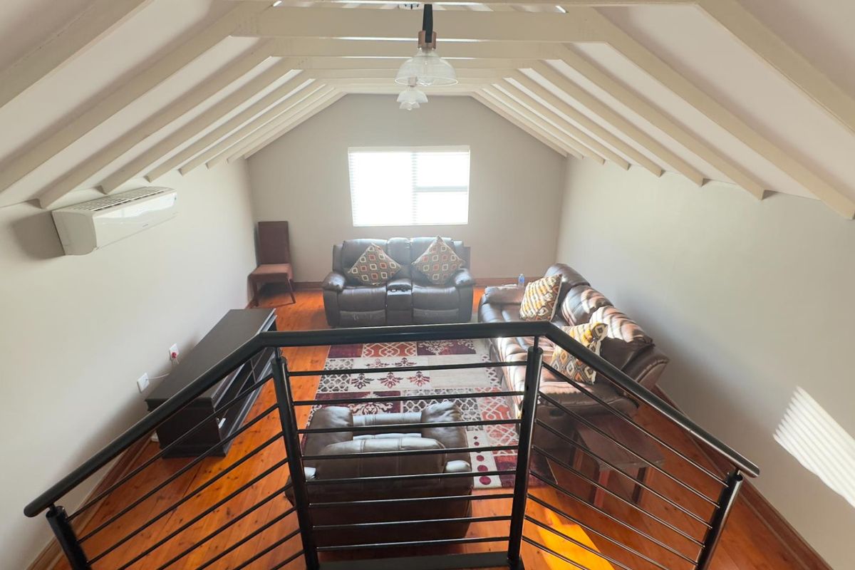 Spacious loft-style living area featuring exposed timber rafters, polished wooden flooring, and a wall-mounted air conditioning unit.