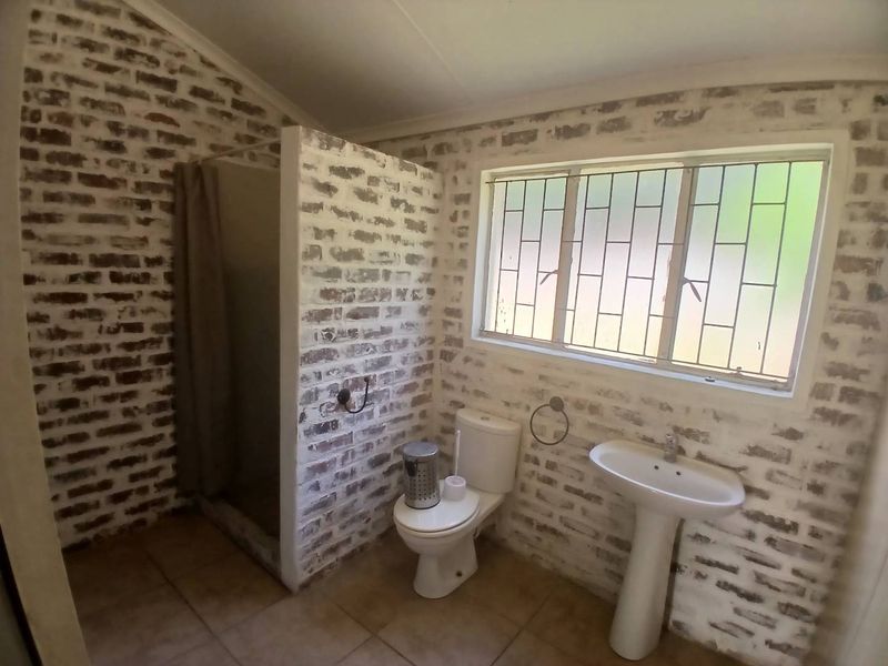 A bathroom featuring exposed brick walls, a pedestal basin, a toilet, and a shower enclosure with security bars on the window.