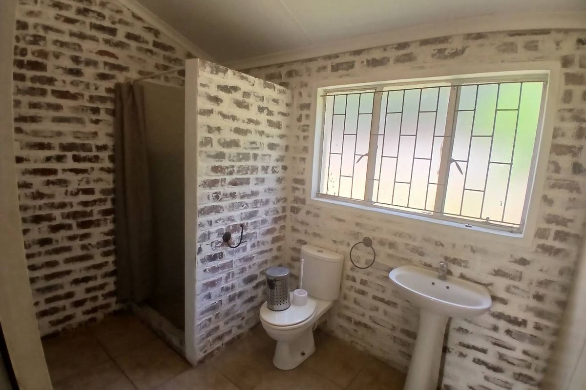 A bathroom featuring exposed brick walls, a pedestal basin, a toilet, and a shower enclosure with security bars on the window.