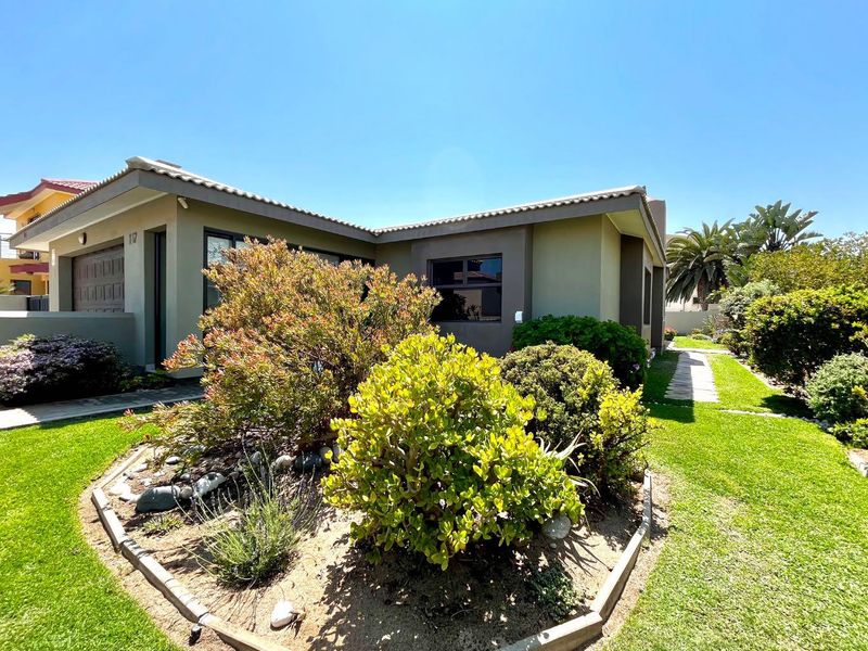 A well-maintained single-story house exterior featuring a landscaped front garden, paved walkway, and integrated garage.